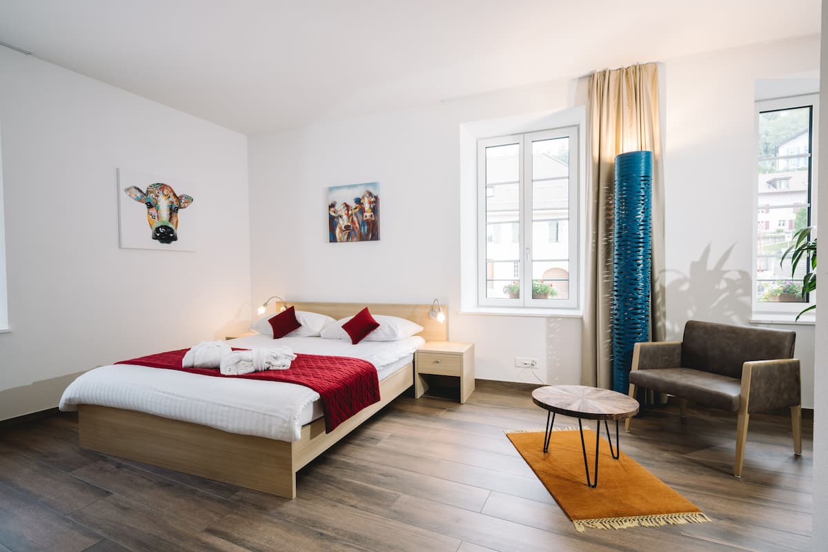 Een moderne hotelkamer met een houten bed, een klein rond tafeltje, een stoel en kunst aan de wanden.