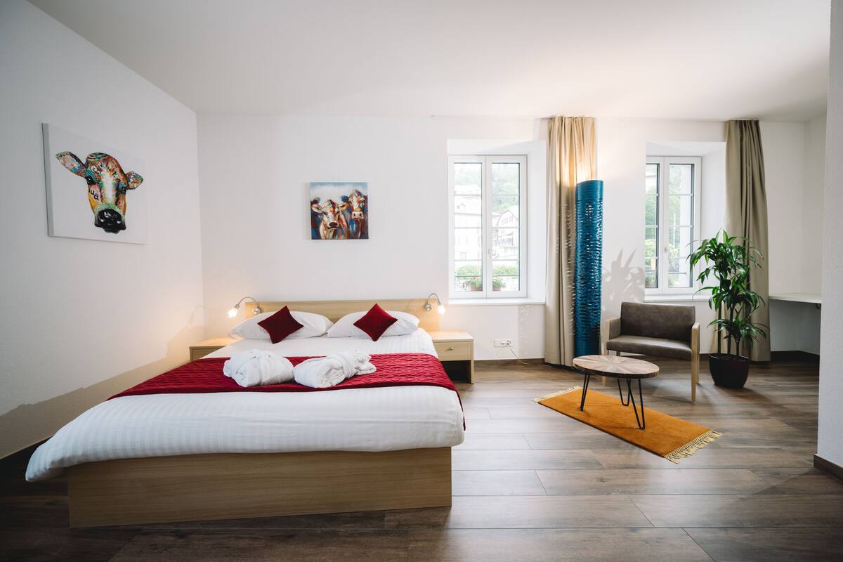 Een hotelkamer met een bed, een stoel, een tafel, een raam en kunstwerken aan de muren.