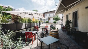 Een terras buiten met tafels en stoelen, plantenpotten en een vat.