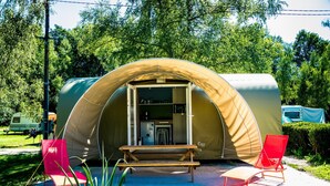 A dome-shaped tent with a built-in kitchenette, a bench, and two red chairs.