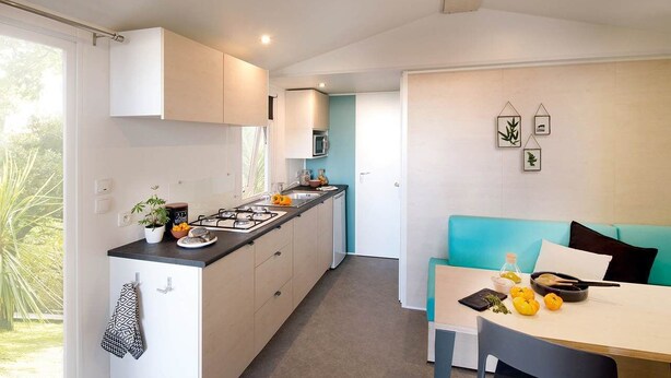 A modern kitchen with white cabinets, a black countertop, and a dining area with a teal sofa and table.