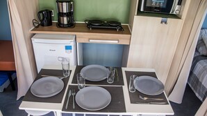 A compact kitchenette with a coffee maker, microwave, and a small refrigerator. There is a dining table set with plates, cutlery, and glasses.