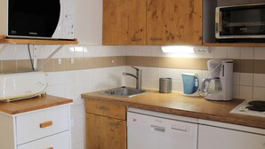 A compact kitchen with wooden cabinets, a white dishwasher, a microwave, a toaster, and a coffee maker.