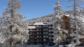 A multi-story hotel with a ski resort backdrop, featuring a clear blue sky and snow-covered trees.