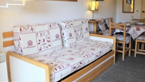 A cozy room with a wooden sofa, a dining table with chairs, and two wall-mounted lamps.
