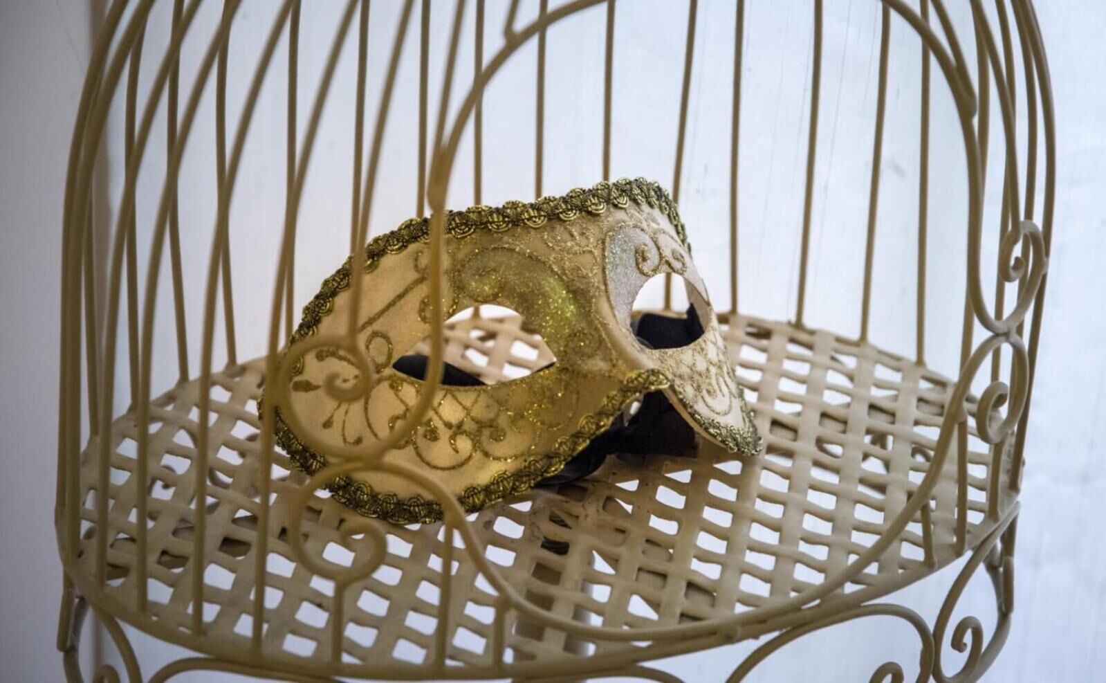 A decorative birdcage with a mask inside.