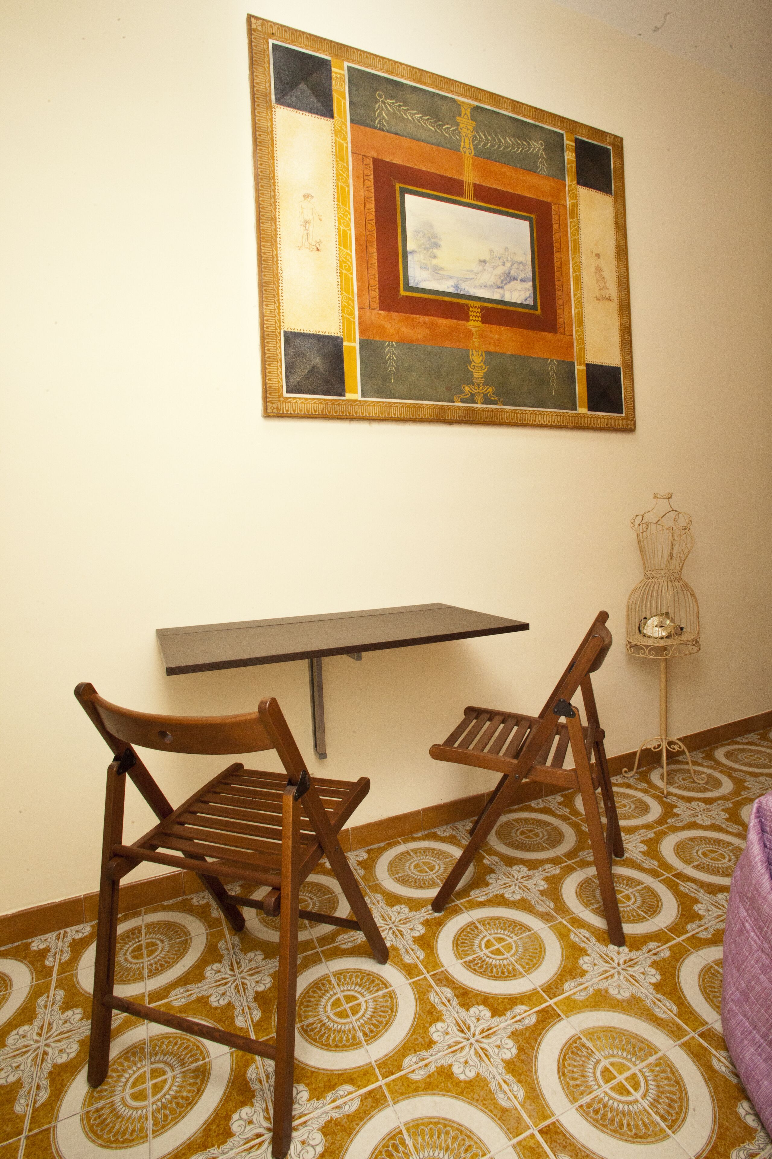 Una habitación con piso estampado, una silla de madera, una mesa y un cuadro en la pared.