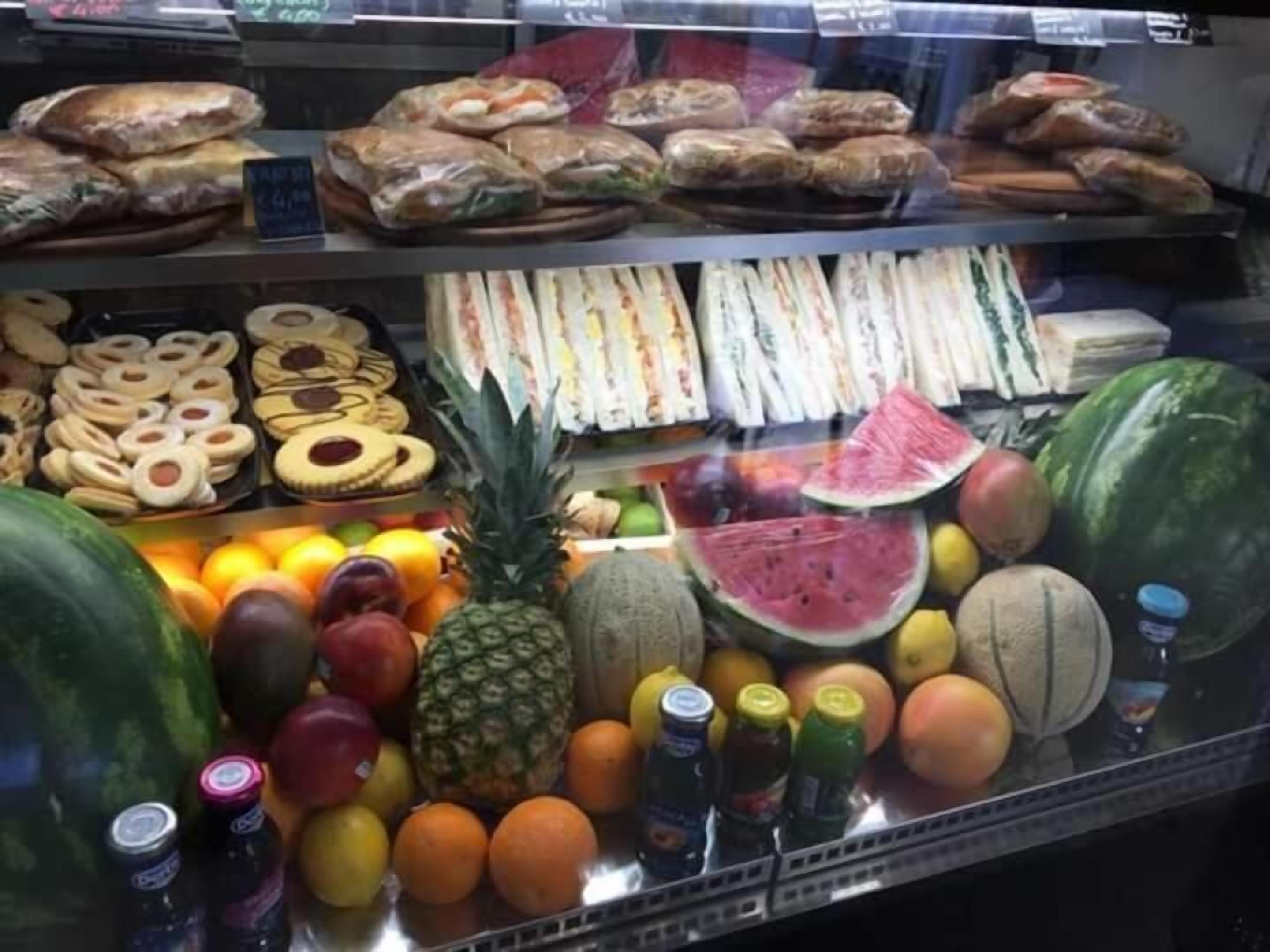 A display case with various food items including sandwiches, pastries, and fruits like watermelon and pineapple.