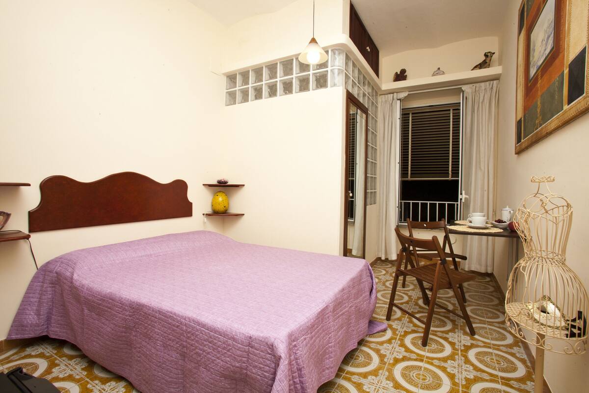 A bedroom with a bed, a chair, a table, and a window.