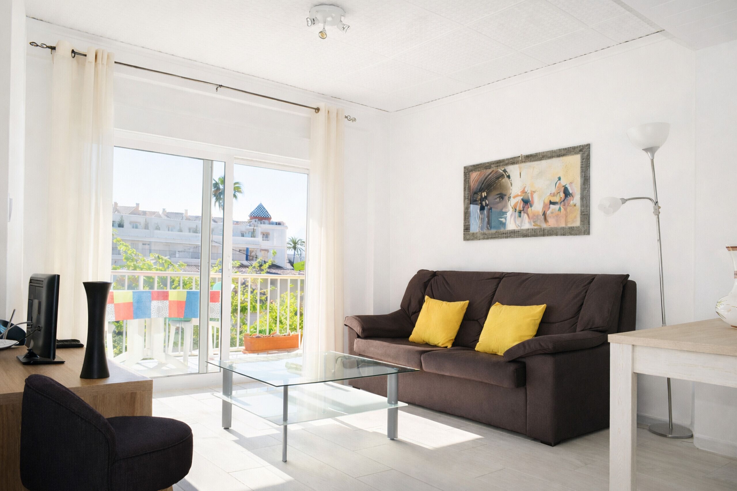 Un salon moderne avec un canapé, une table basse en verre, un bureau et un tableau accroché au mur.