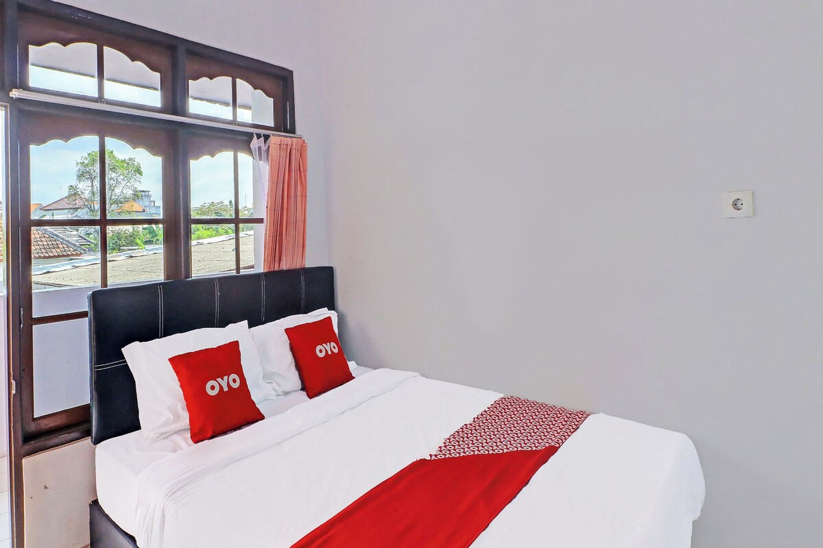 A neatly made bed with white and red bedding, a black headboard, and a window with curtains.