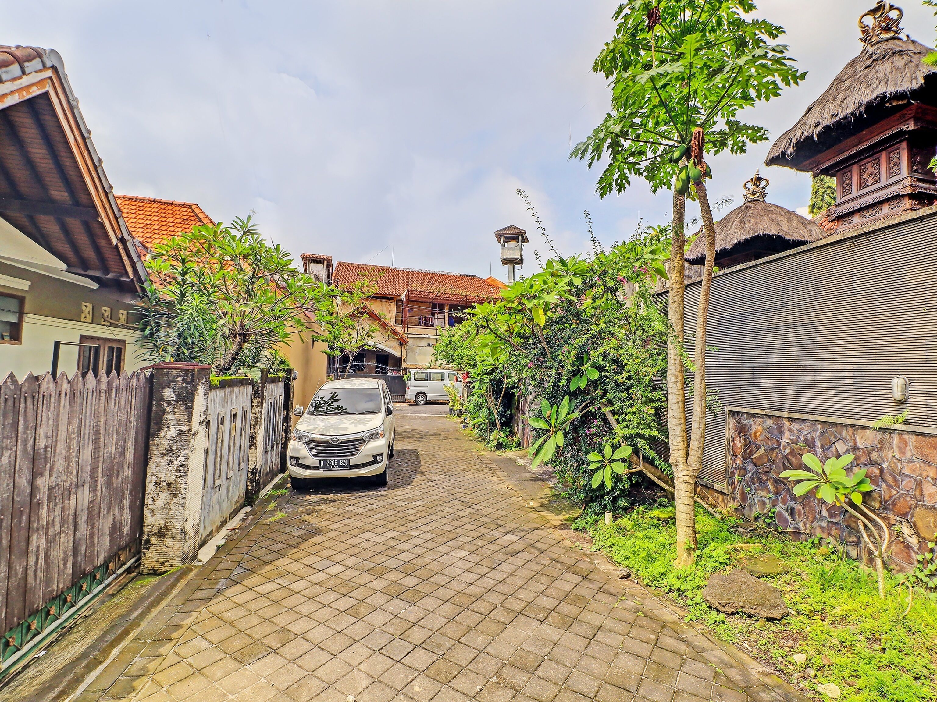 A narrow cobblestone street flanked by traditional buildings with thatched roofs and lush greenery.