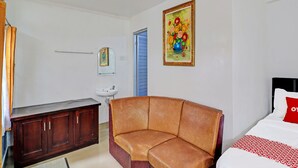 Hotelkamer met een bruine leren bank, een bed met een rood kussen, een witte wasbak, een houten kast, een spiegel en een schilderij van bloemen aan de muur.