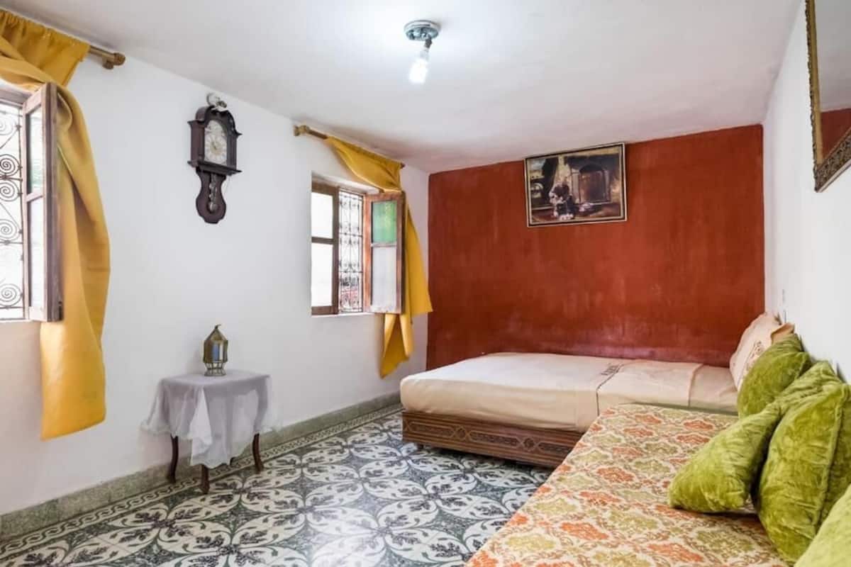 Une pièce comprenant un lit, une petite table avec une lanterne, une horloge murale et un tableau.