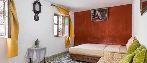 Una habitación con una cama, una mesita con un farol, un reloj de pared y un cuadro.