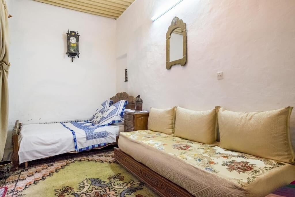 Een kamer met een bed, een slaapbank, een kamerkleed met dessin, een wandklok en een spiegel.