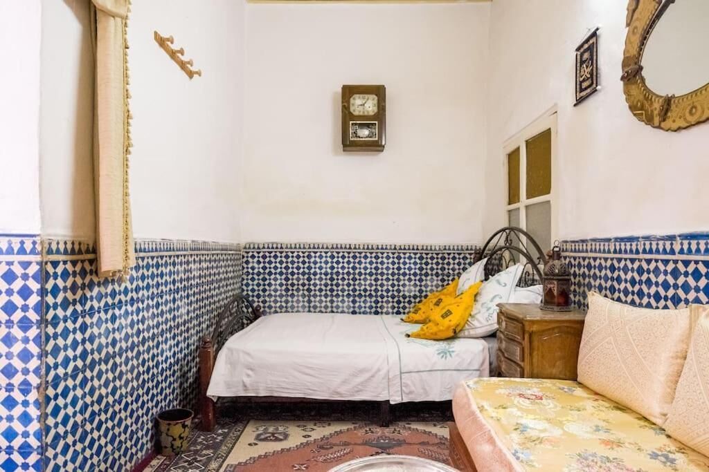 Una habitación con una cama, una mesita y un reloj de pared.