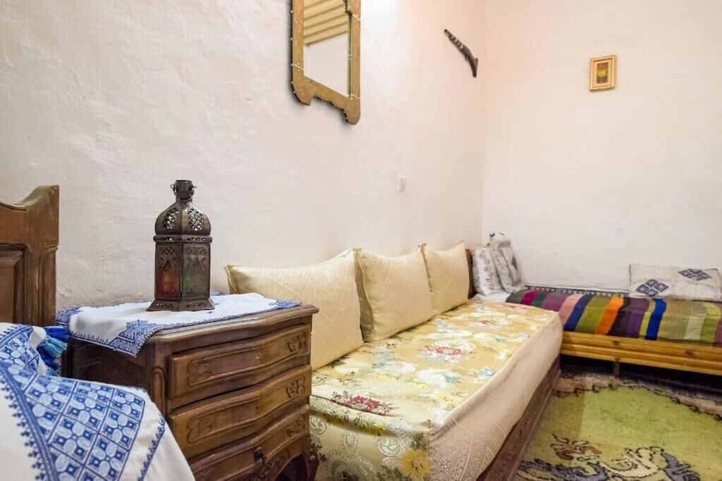Un dormitorio con un aparador de madera, una cama con colcha estampada, una mesita con un farol y un espejo en la pared.