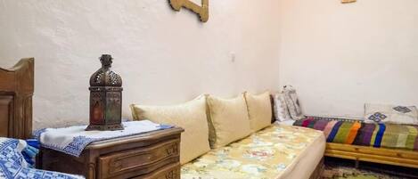 Un dormitorio con un aparador de madera, una cama con colcha estampada, una mesita con un farol y un espejo en la pared.