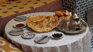 A round table with a white tablecloth, various dishes, bread, and a silver teapot. - Dar Fatimazahra (Fes)