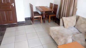 Una sala de estar con sofá, una mesa de centro, una mesa de comedor y sillas, y una puerta.