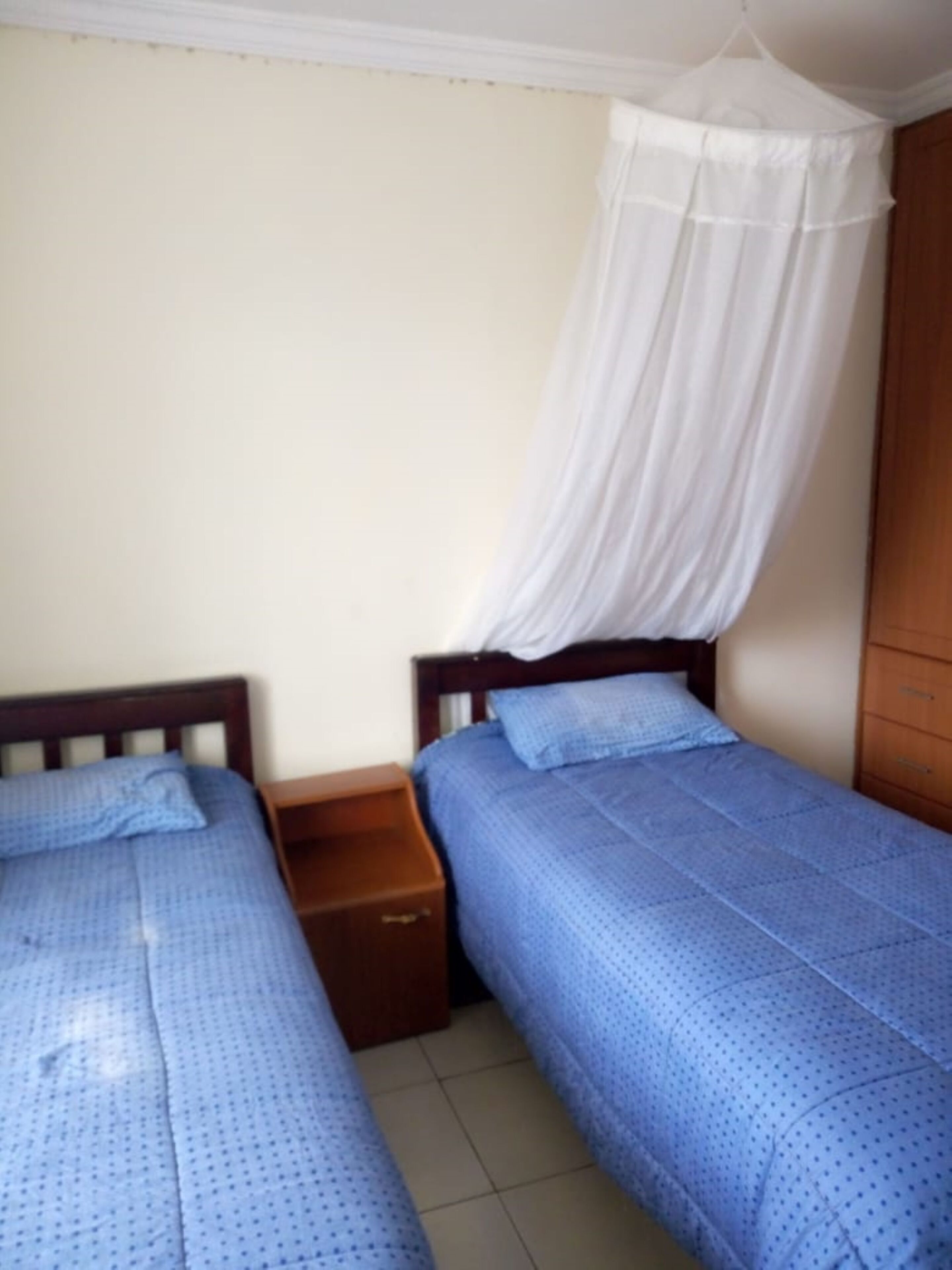 Un dormitorio con dos camas individuales, un armario de madera y una mesita de noche.