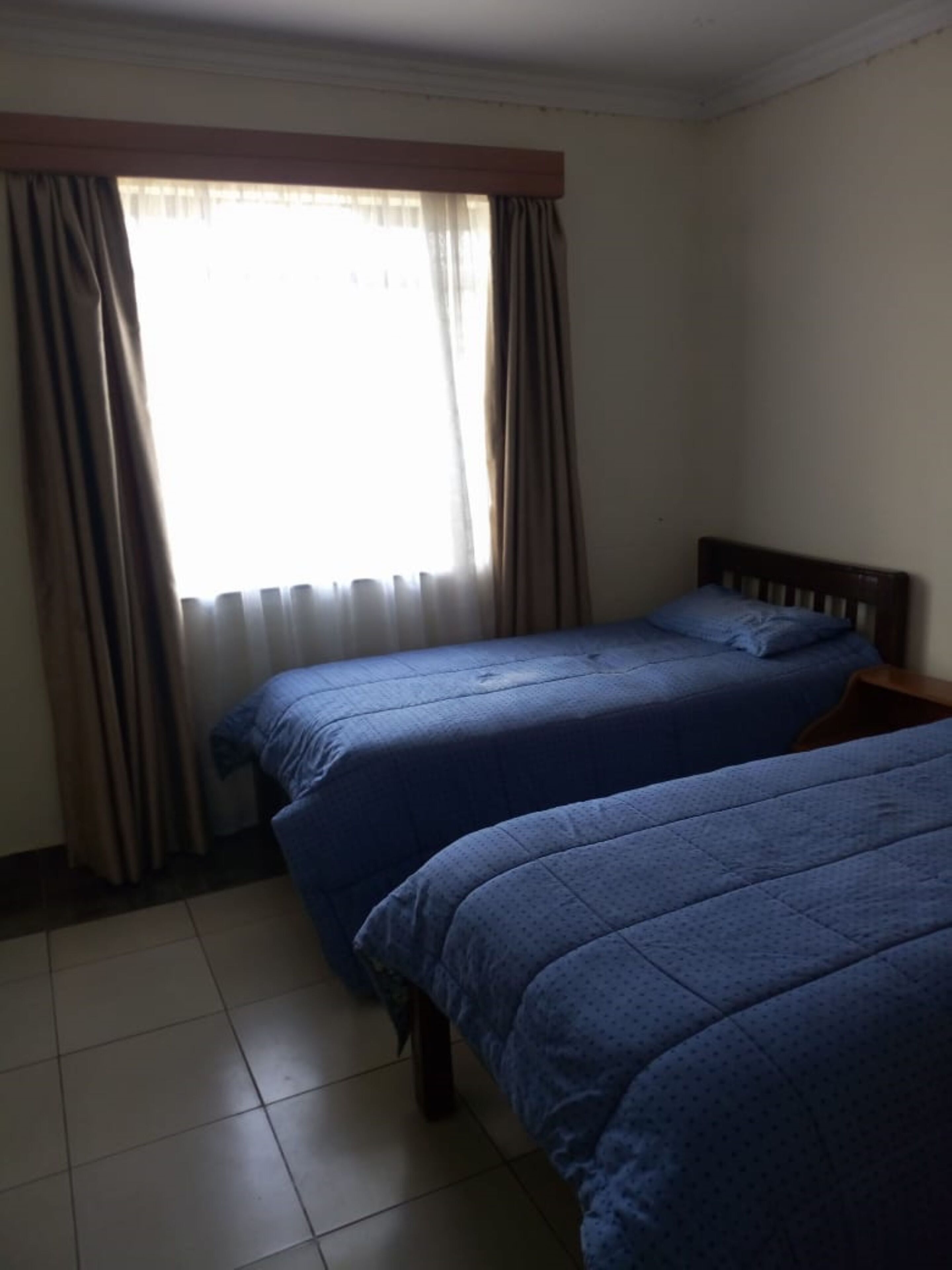 A room with two beds, a window with curtains, and a wooden headboard.