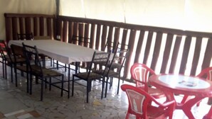 Un área de comedor al aire libre techada con piso de mosaico, una mesa larga con sillas y una mesa más pequeña con sillas rojas.