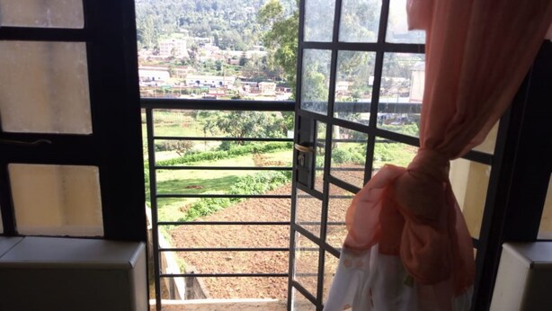 Vista a través de una ventana con celosía de metal, cortina y suelo de baldosas.