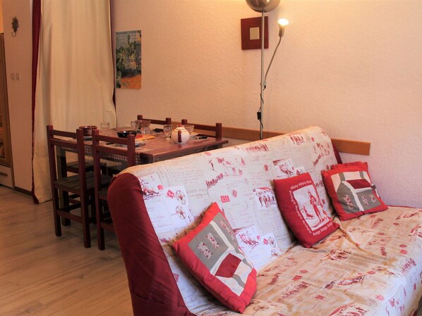 Un salon chaleureux avec une table à manger en bois, un canapé agrémenté de coussins à motifs et une lampe fixée au mur.