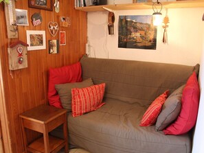 Une pièce chaleureuse avec un mur en bois, un canapé marron agrémenté de coussins rouges et gris, une petite table en bois et divers éléments de décoration murale, notamment des tableaux et un ornement en forme de cœur.
