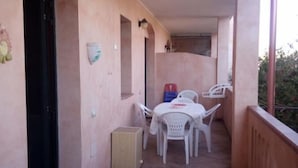 Un balcón con suelo de baldosas, una mesa con sillas y una puerta.