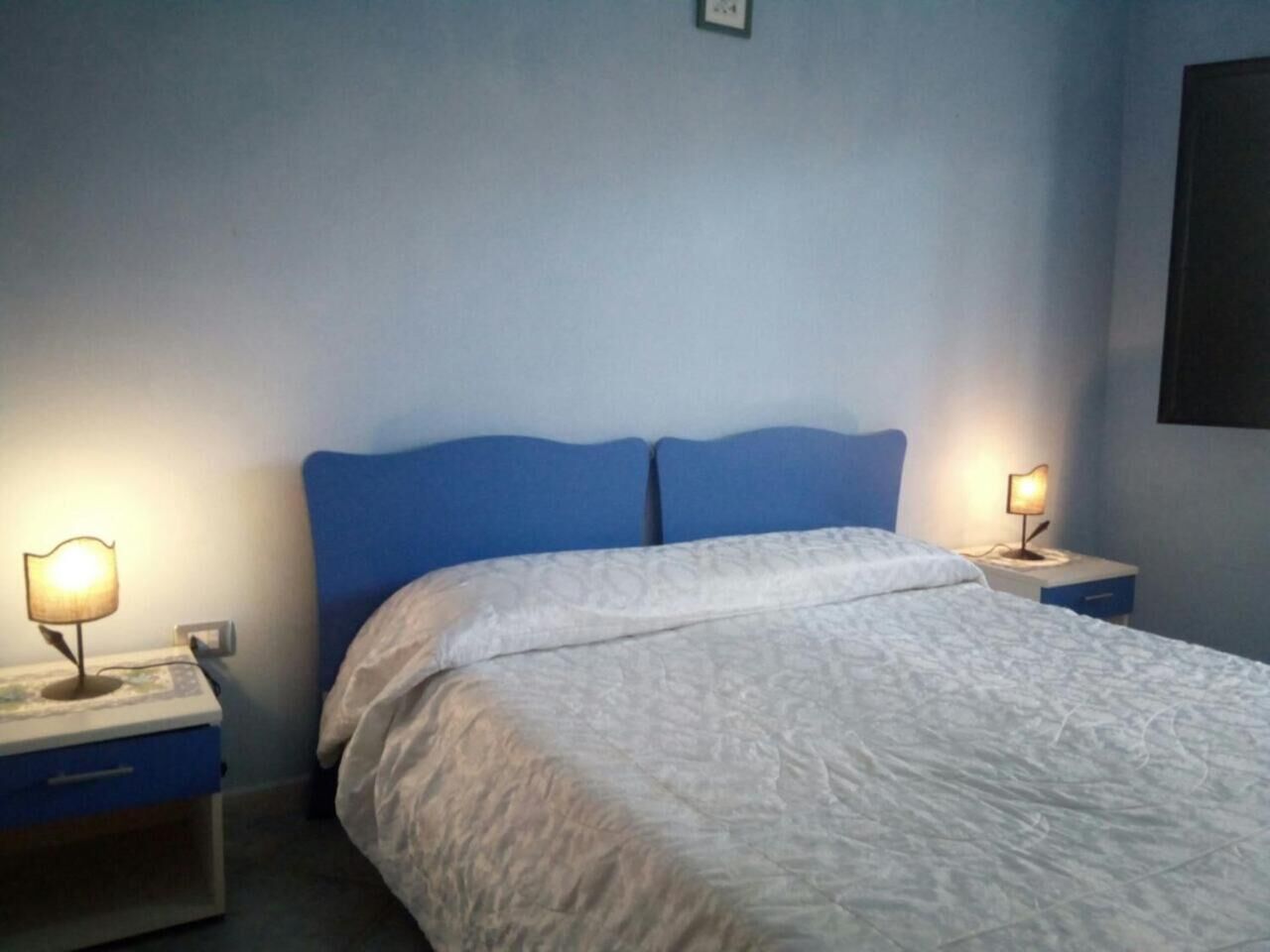 A neatly made bed with a white comforter and two pillows, flanked by two bedside tables with lamps.