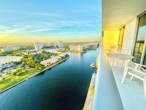A balcony with a view of a river, buildings, and a boat.