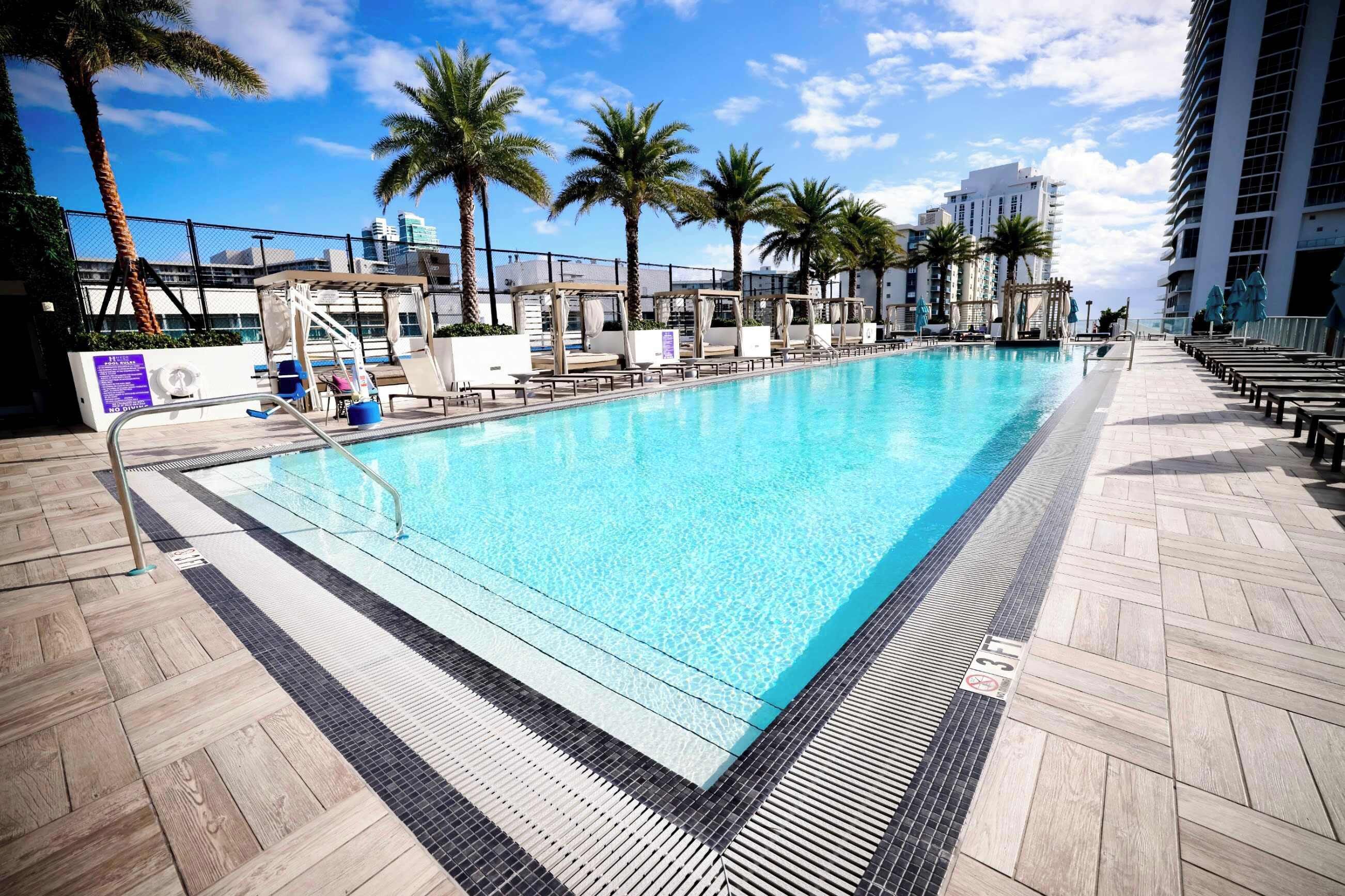 A swimming pool with a tiled deck, palm trees, and a cityscape in the background.