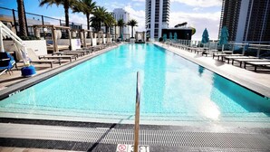 A swimming pool with a no diving sign, surrounded by palm trees and modern buildings.