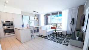 A modern apartment with a kitchen, dining area, and living room. It features a large window with a city view, a sofa, and a coffee table.