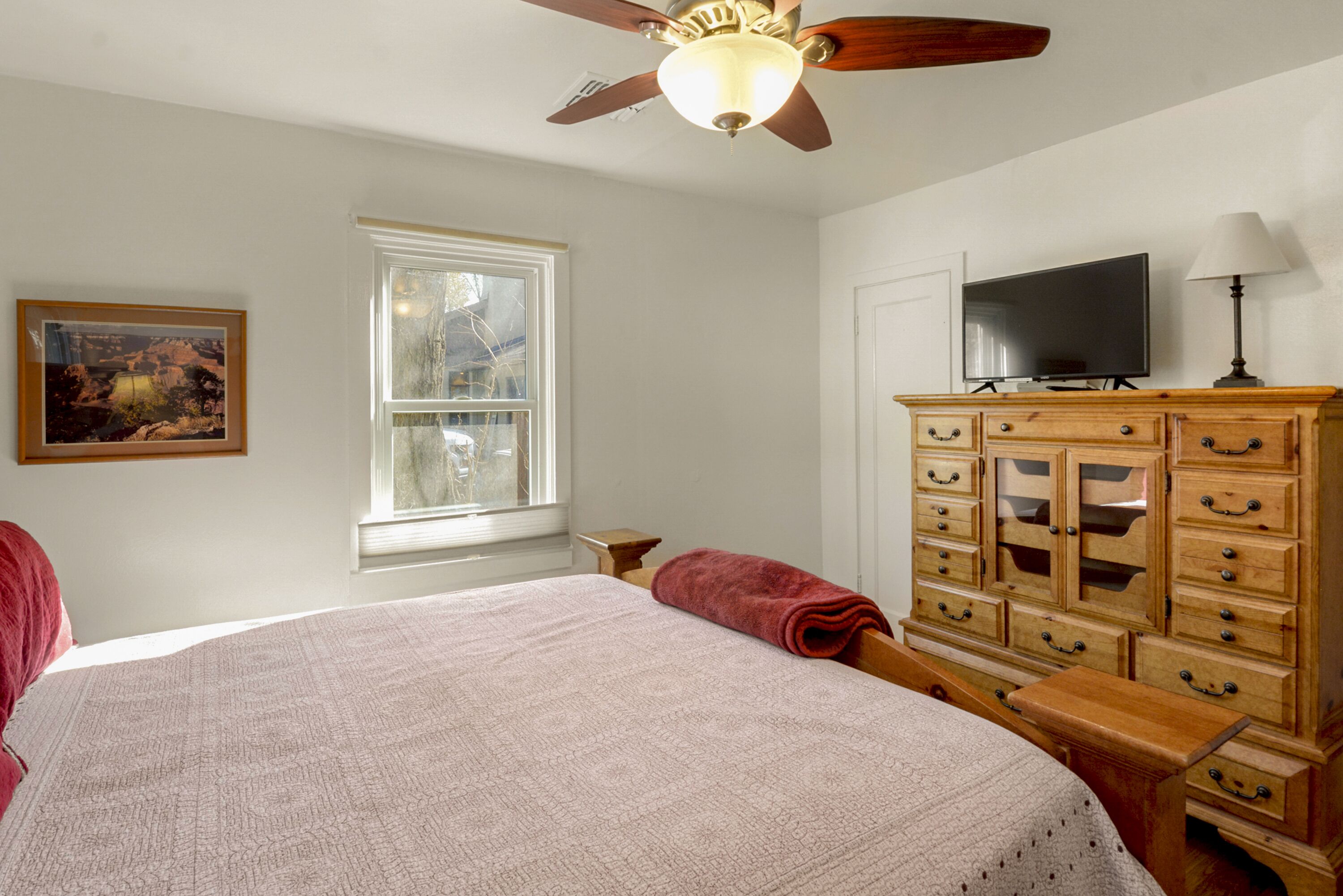 A bedroom with a bed, a wooden dresser, a television, and a window.