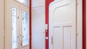A hallway with two white doors, one with a frosted glass window and another with a plain glass window. The walls are painted red, and the floor is wooden. - Akacfa 18 Apartment (Budapest)
