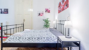 A neatly made bed with a patterned bedspread, a bedside table with a lamp, and a wall with framed pictures. - Akacfa 18 Apartment (Budapest)