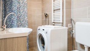 A modern bathroom with a washing machine, toilet, and a tiled shower area. - Akacfa 57 Apartment II. (Budapest)