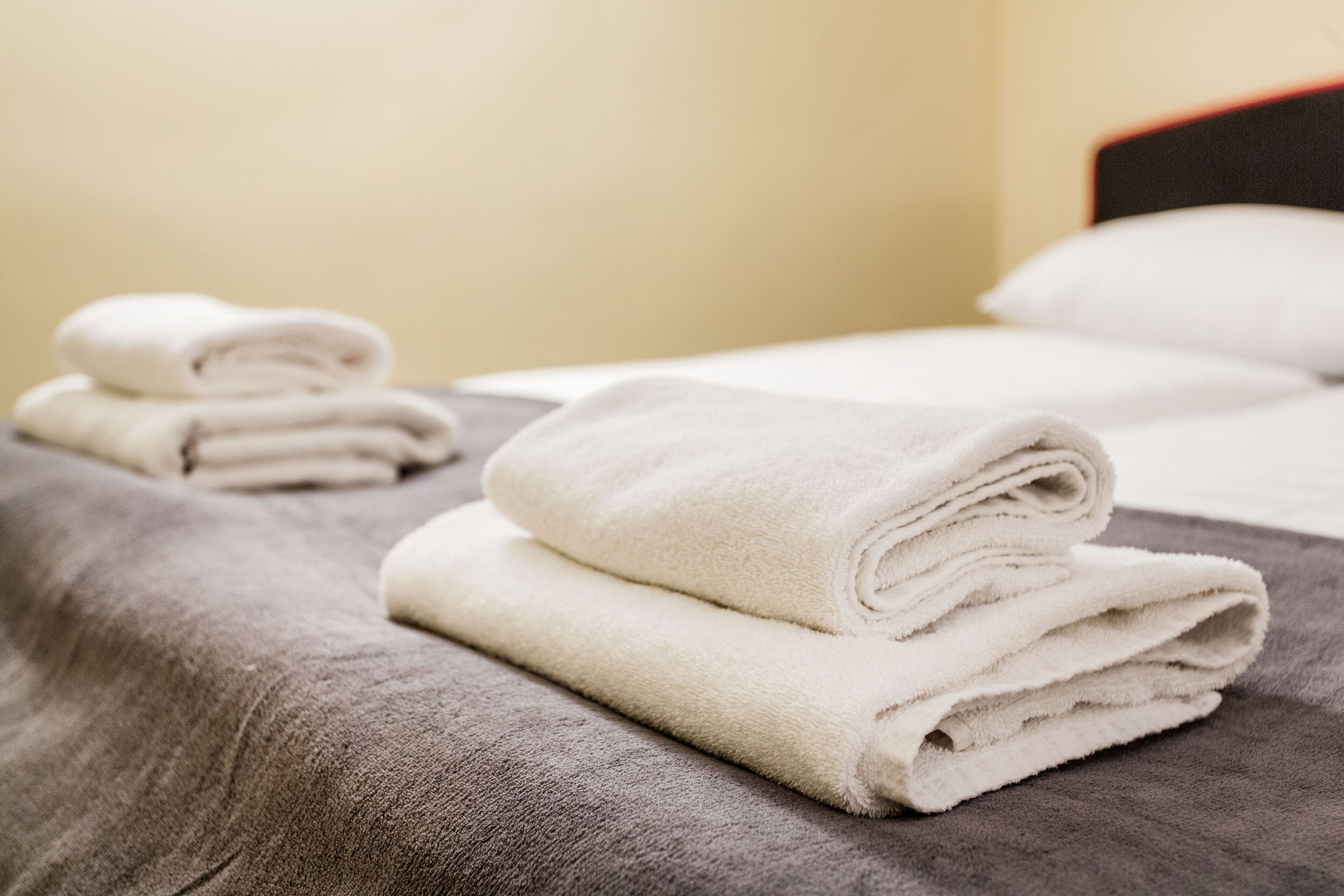 A neatly made bed with folded white towels and a grey blanket.