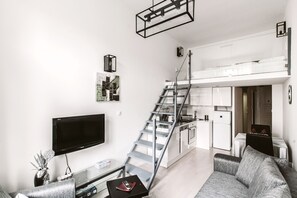 A modern apartment with a living room, a dining area, a kitchen, and a staircase.