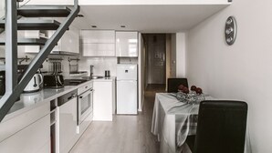 A modern kitchen with white appliances, a dining area with a table set for two, and a staircase leading to an upper level. - Andrassy 1 Apartment (Budapest)