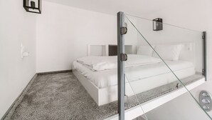 A modern bedroom with a glass partition bed, white bedding, and a small bedside table with a clock. - Andrassy 1 Apartment (Budapest)