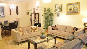 A living room with two sofas, a coffee table, a dining table with chairs, a bookshelf, and a large potted plant. - Bajcsy 1 Apartment (Budapest)