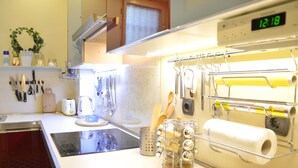 A kitchen with a digital clock displaying 12:18, a kettle, a toaster, and utensils hanging on the wall. - Bajcsy 1 Apartment (Budapest)