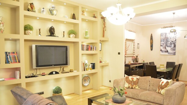 A living room with a flat-screen TV, a sofa, a coffee table, and a dining area with a glass table and chairs. - Bajcsy 1 Apartment (Budapest)