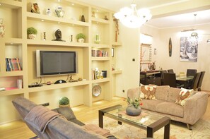 A living room with a flat-screen TV, a sofa, a coffee table, and a dining area with a glass table and chairs. - Bajcsy 1 Apartment (Budapest)