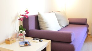 En stue med en lilla sofa, et hvidt sofabord og et lille bord med en plante og en bog.